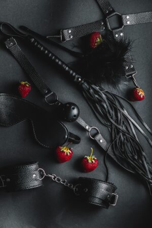 Black leather BDSM accessories with strawberries on a dark background. Captivating and intriguing composition.